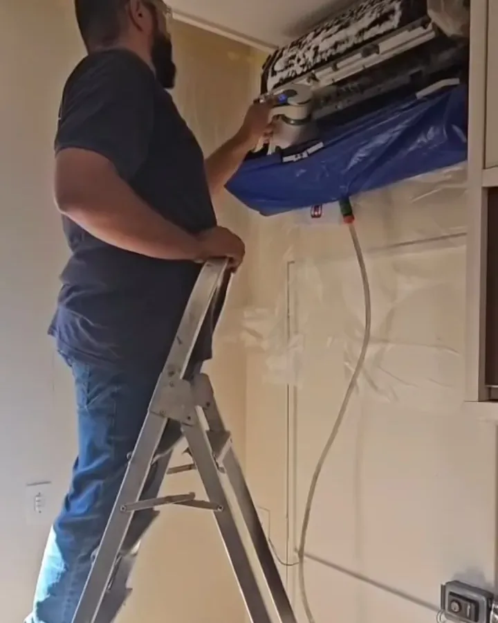 Técnico na escada desmontando o ar condicionado com a bolsa coletora azul instalada