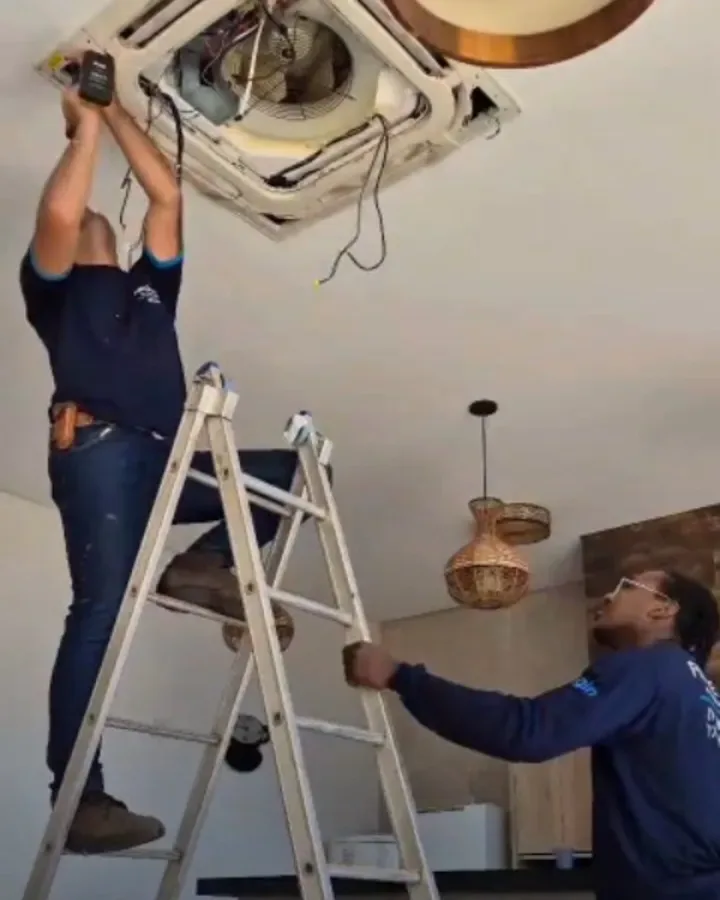Técnicos fazendo a manutenção de um ar condicionado cassete no teto de um comércio